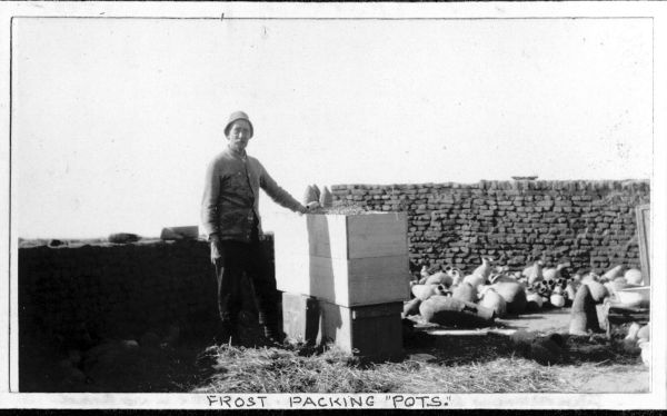 Image of Mr Frost with wooden boxes and a pile of Egyptian pots. A handwritten caption reads 'FROST PACKING 