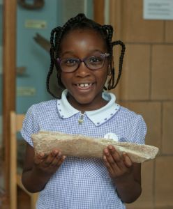 School girl holds fossil in Art Gallery during visit, smiling.