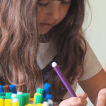 A girl concentrates as she draws on a wooden dowel.