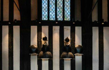 A photo taken inside the medieval Great Hall showing suits of armour displayed on the timber-framed wall.