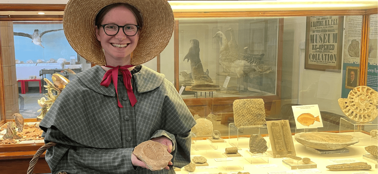 A photo of someone dressed as Mary Anning holding out a fossil at Worcester City Art Gallery and Museum.