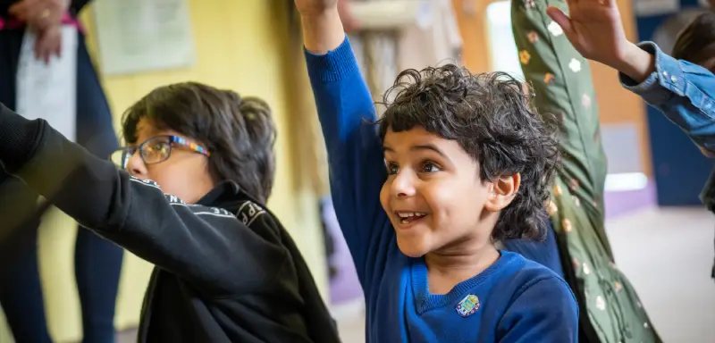 Two children enthusiastically with hands up to answer a question.