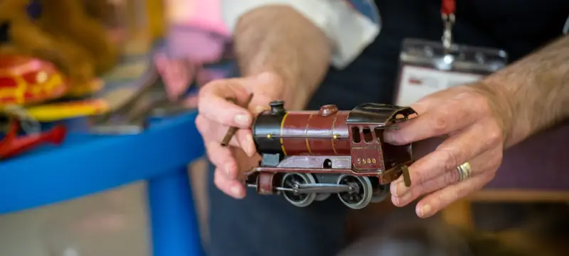 A photo showing a man's hands holding up a toy train from the museum's collection.