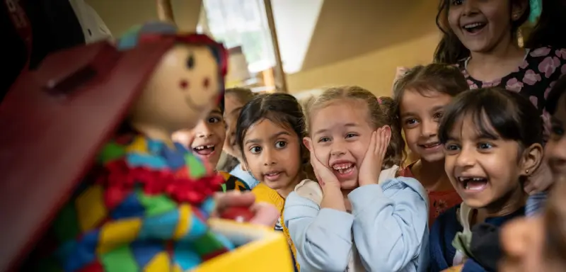 A group of children excitedly watching a jack-in-the-box pop up in the museum.