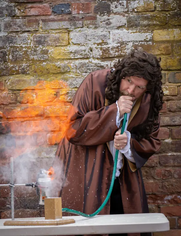 A man dressed as Pepys blowing through a pipe to create flames.