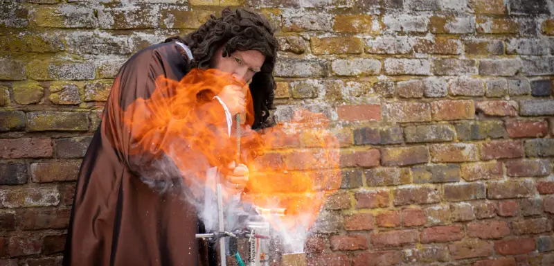 A man dressed as Pepys blowing through a pipe to create flames.